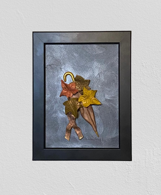 Autumn wall frame. It portraits four leaves in bronze, golden brown and olive green with an bronze umbrella.  All of the elements are in 3D form and crafted with polymer clay. The background is painted in industrial gray and the frame is black.