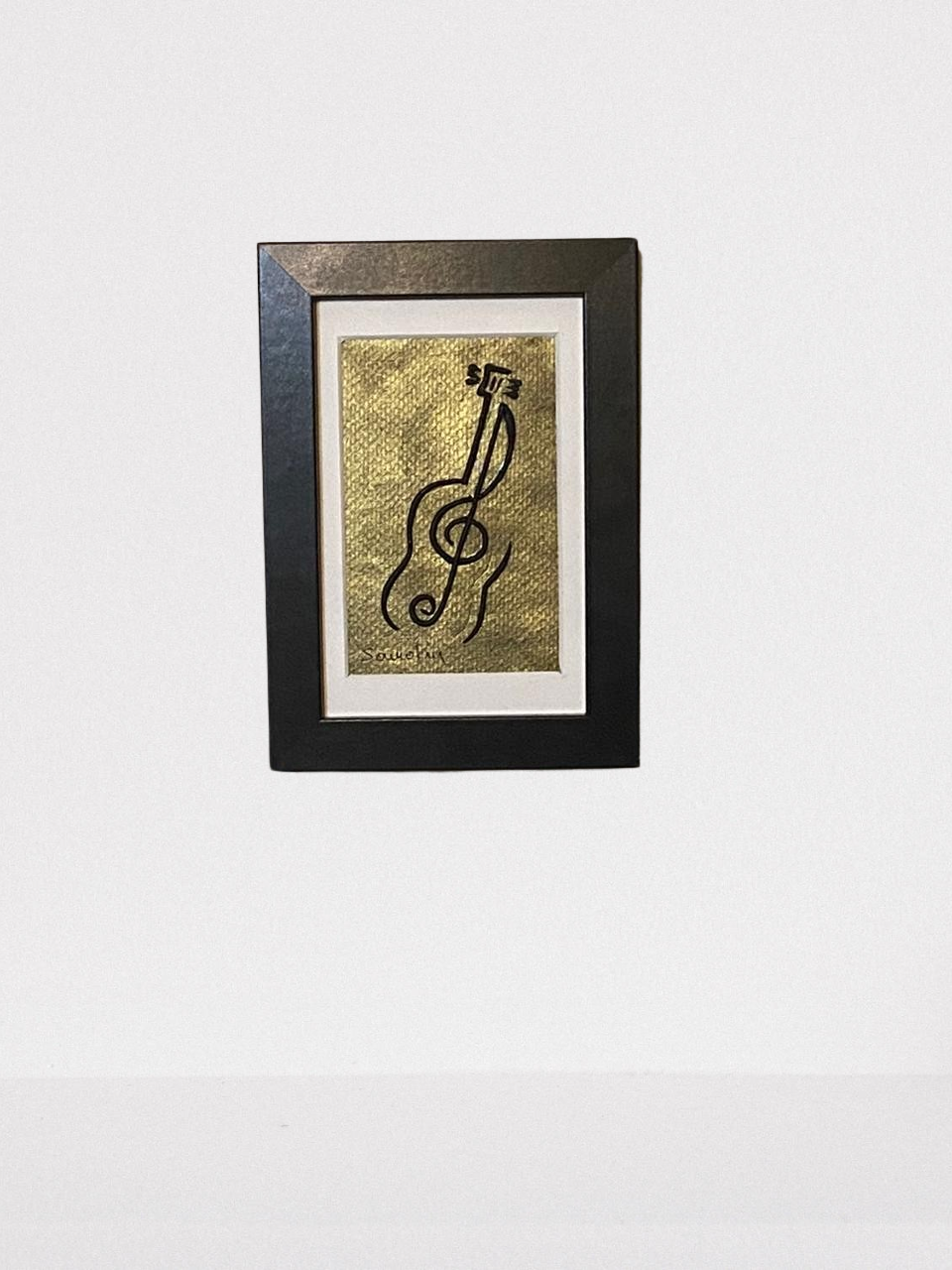 Handmade wall frame, featuring a 3D guitar crafted with polymer clay on a golden painted canvas. The frame is white and made of wood.