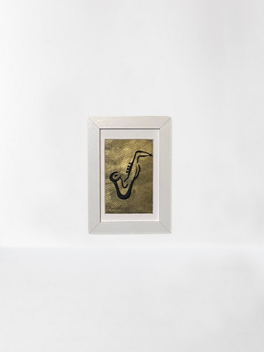 Handmade wall frame, featuring a 3D saxophone made with polymer clay on a golden painted canvas. The frame is white and made of wood.