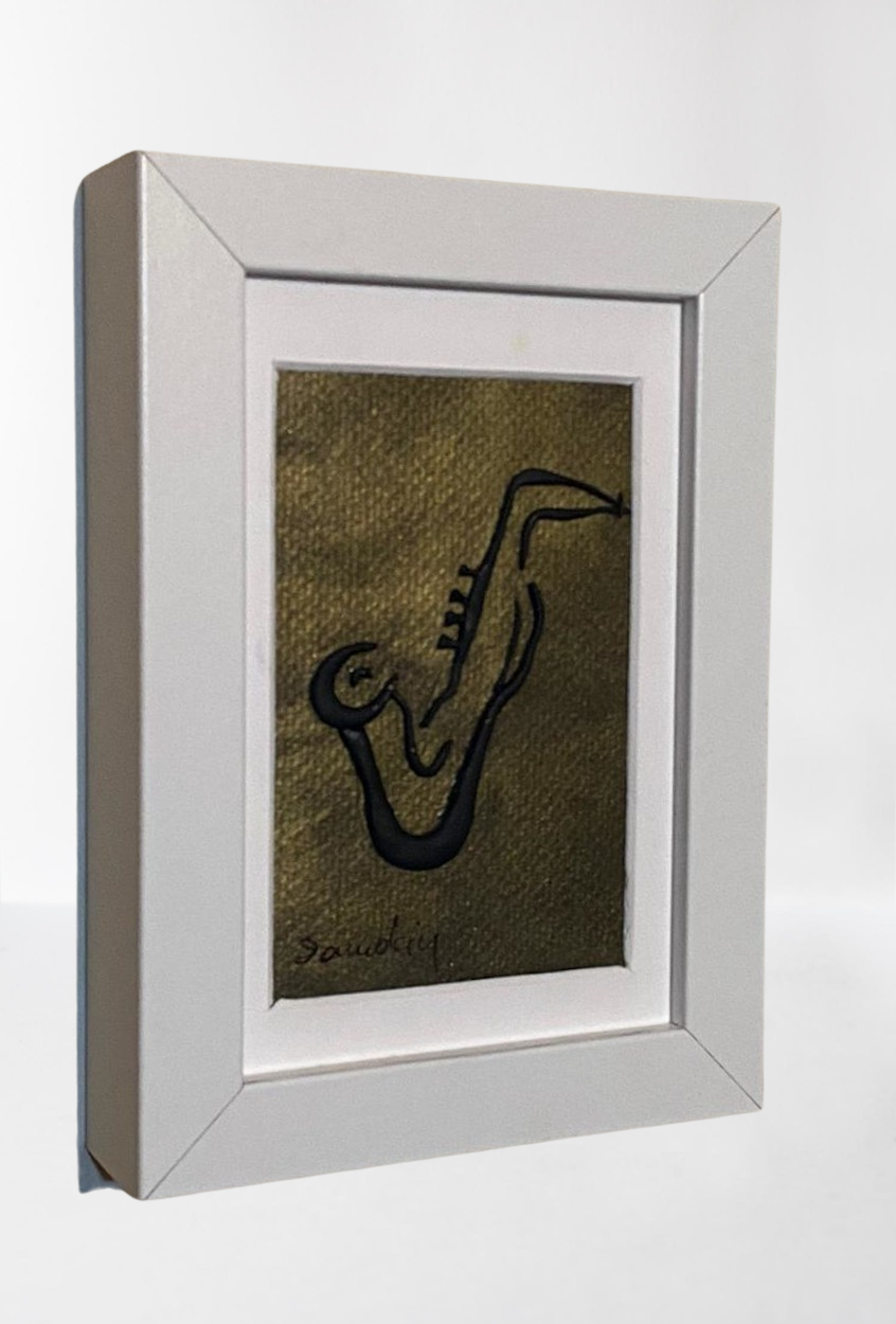 Handmade wall frame, featuring a 3D saxophone made with polymer clay on a golden painted canvas. The frame is white and made of wood.